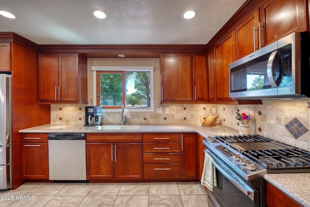 kitchen with backsplash, stainless steel appliances, a sink, and brown cabinetry