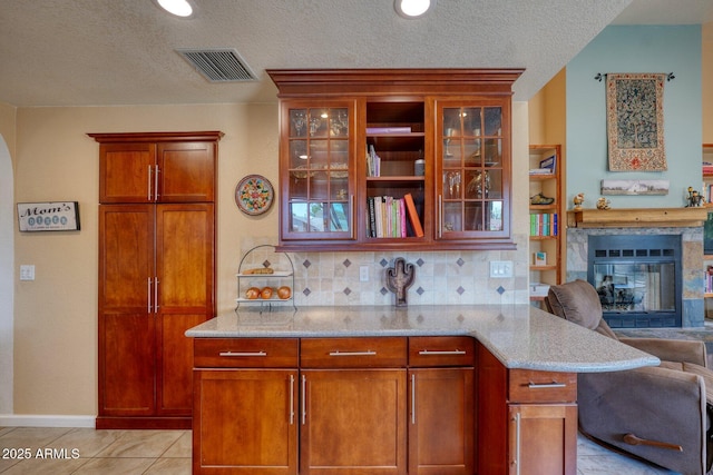 kitchen featuring light tile patterned flooring, visible vents, open floor plan, backsplash, and light stone countertops