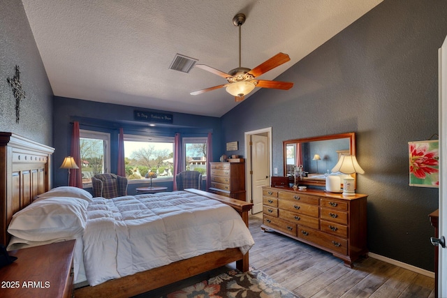 bedroom with visible vents, a textured wall, vaulted ceiling, a textured ceiling, and wood finished floors