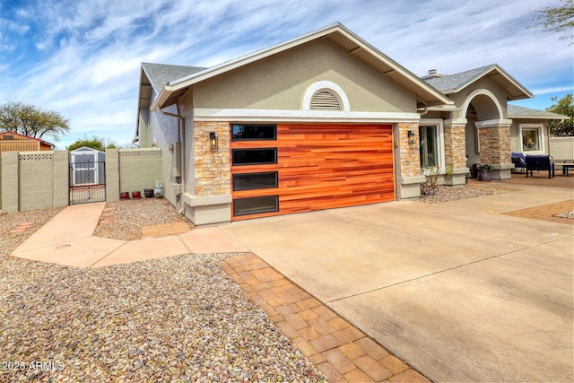 view of front of house featuring stone siding, a gate, concrete driveway, and stucco siding