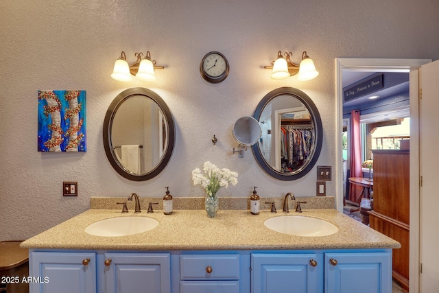 full bathroom with a textured wall, double vanity, and a sink