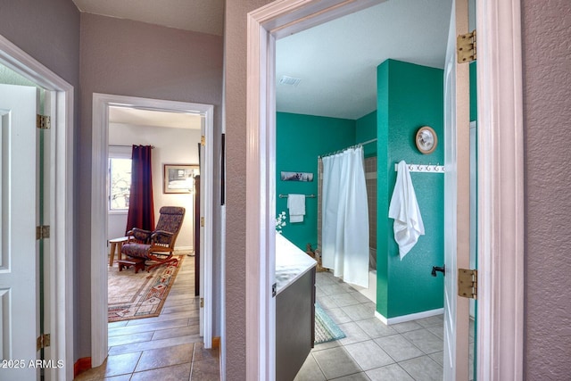 full bath featuring a textured wall, tile patterned flooring, and baseboards