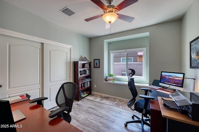 office area with ceiling fan, a textured ceiling, visible vents, baseboards, and light wood-style floors