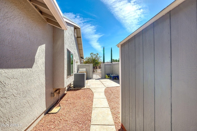 view of side of home with a gate, stucco siding, fence, and central AC unit