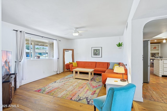 living area with arched walkways, a ceiling fan, and wood finished floors