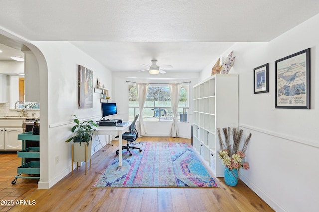 office with arched walkways, baseboards, a sink, and light wood finished floors