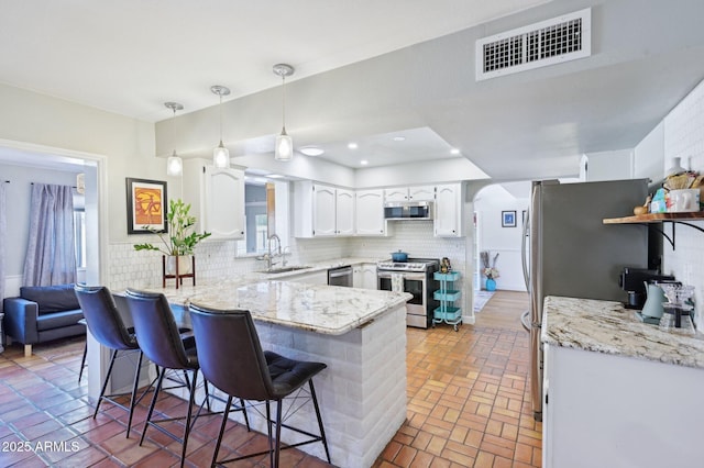 kitchen featuring stainless steel appliances, a peninsula, a sink, visible vents, and white cabinets