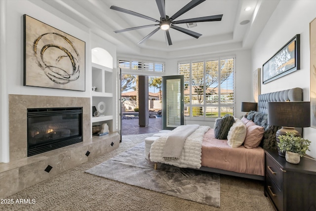 bedroom featuring ceiling fan, a high end fireplace, and a tray ceiling