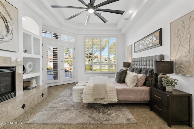 bedroom featuring french doors, access to exterior, a tray ceiling, ceiling fan, and a fireplace