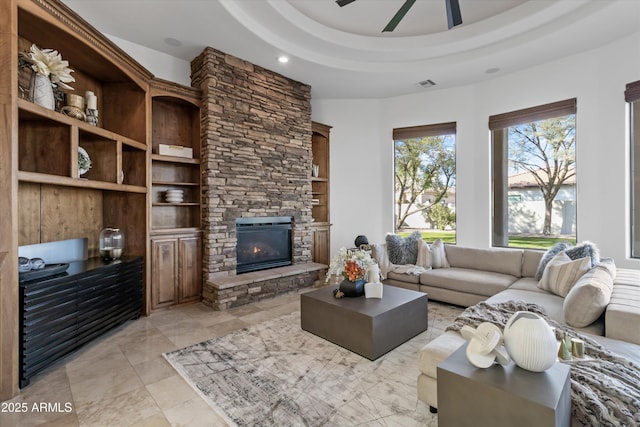 living room featuring ceiling fan, a fireplace, and a tray ceiling