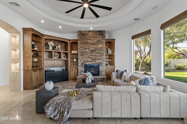 living room with a stone fireplace and a raised ceiling