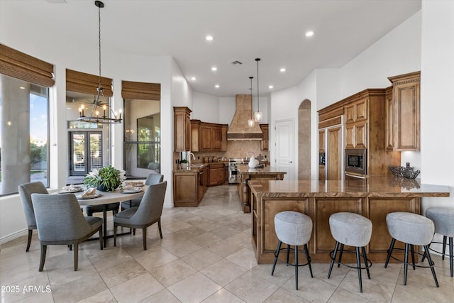 kitchen featuring dark stone countertops, hanging light fixtures, built in appliances, custom exhaust hood, and kitchen peninsula