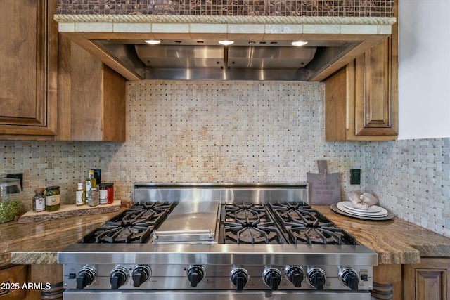 kitchen featuring wall chimney range hood, stainless steel stove, and decorative backsplash