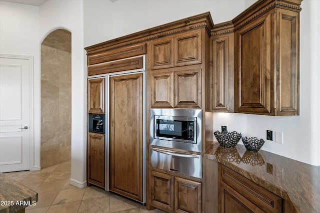 kitchen featuring built in appliances, dark stone countertops, and light tile patterned flooring