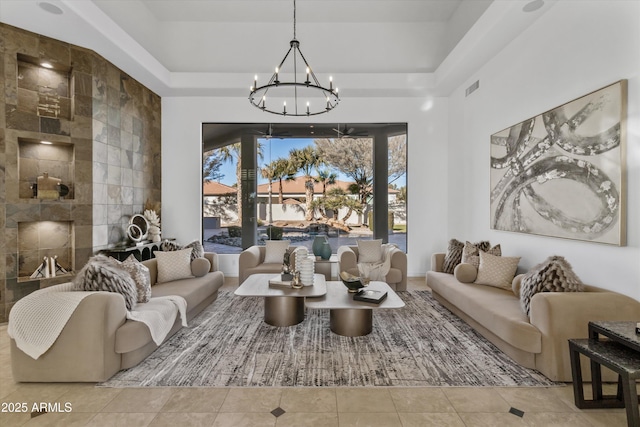 tiled living room with a raised ceiling, a tiled fireplace, and an inviting chandelier