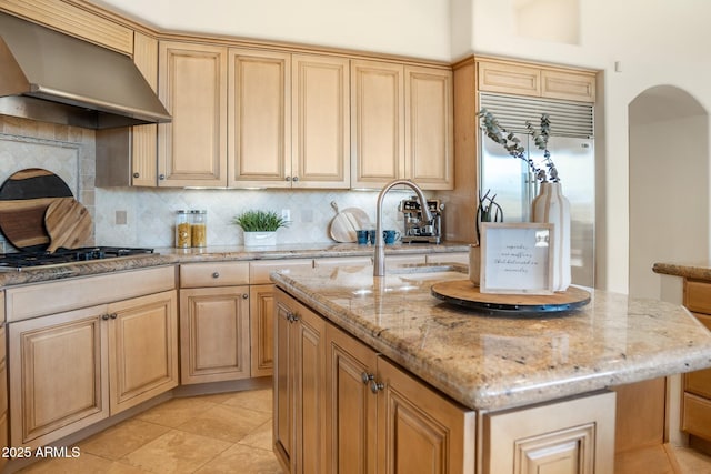 kitchen featuring built in fridge, gas stovetop, decorative backsplash, wall chimney range hood, and light stone countertops