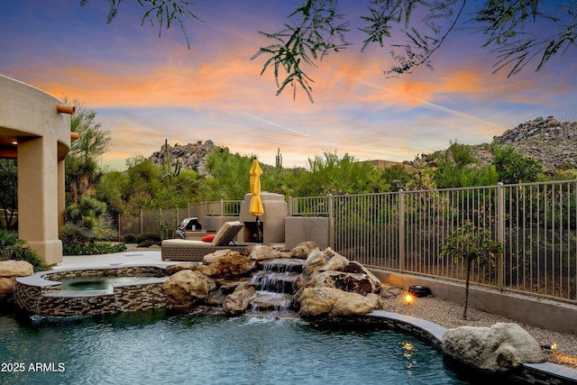 pool at dusk with fence and an in ground hot tub