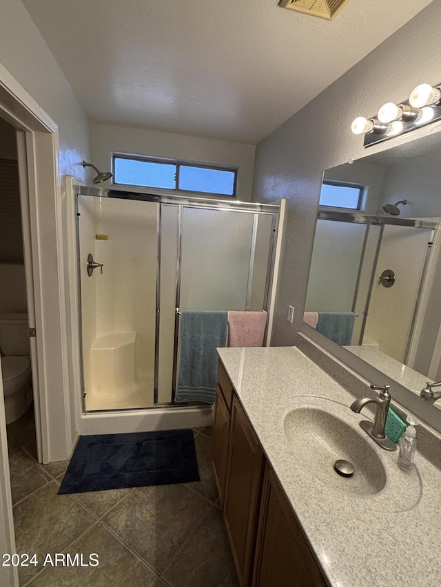 bathroom featuring vanity, a shower with shower door, tile patterned floors, and toilet