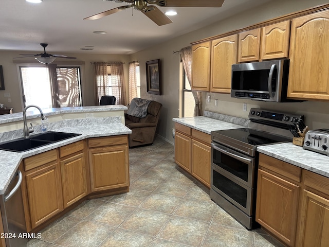 kitchen featuring ceiling fan, stainless steel appliances, light stone countertops, and sink