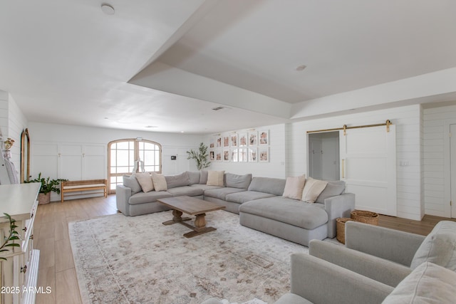 living area featuring light wood-type flooring, a barn door, and wooden walls