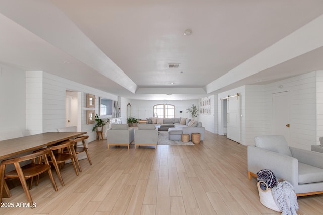 living area featuring visible vents, a barn door, light wood finished floors, and a tray ceiling