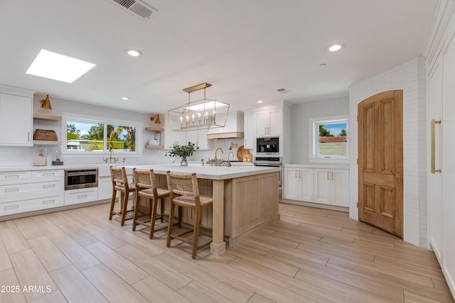 kitchen with open shelves, custom exhaust hood, stainless steel oven, light countertops, and backsplash