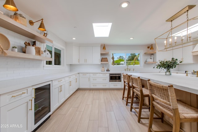 kitchen featuring decorative backsplash, a breakfast bar area, a skylight, open shelves, and white cabinetry