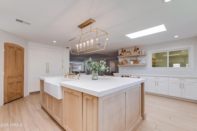 kitchen featuring a sink, light wood-style floors, light countertops, an island with sink, and visible vents