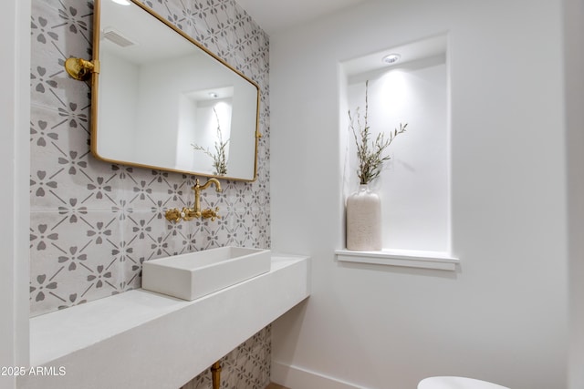 half bathroom with visible vents, decorative backsplash, toilet, baseboards, and a sink