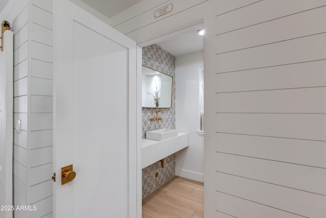 bathroom with wallpapered walls, a sink, and wood finished floors