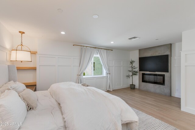 bedroom featuring a fireplace, a decorative wall, light wood-style flooring, recessed lighting, and visible vents