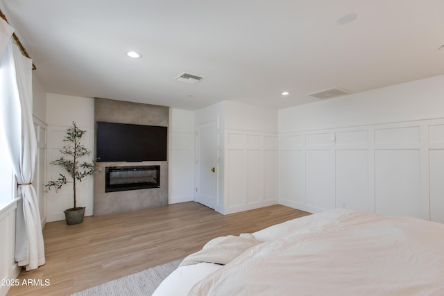 bedroom featuring visible vents, a large fireplace, light wood-type flooring, a decorative wall, and recessed lighting