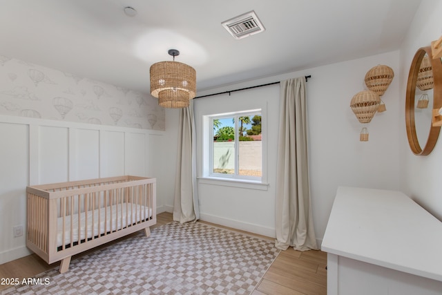 bedroom with a nursery area, visible vents, wainscoting, and wood finished floors