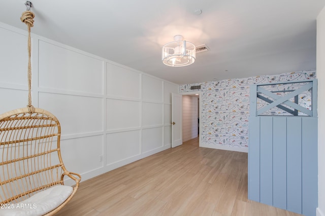 unfurnished room with wood finished floors, a notable chandelier, a decorative wall, and visible vents