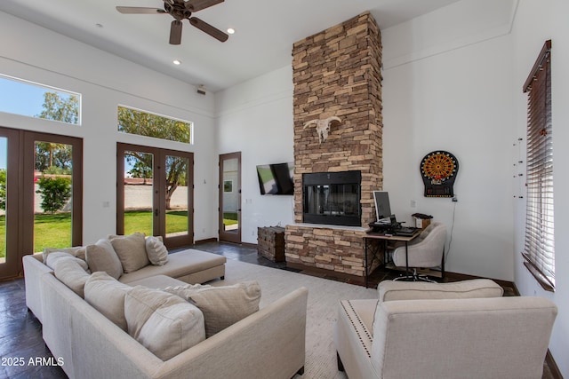 living area with dark wood-type flooring, a ceiling fan, a towering ceiling, and a fireplace