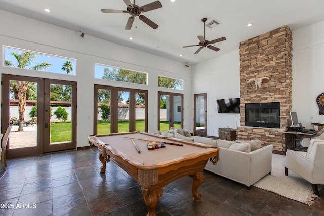 rec room with stone tile floors, a ceiling fan, french doors, and a fireplace