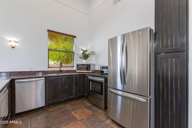 kitchen with a sink, stone finish flooring, dark brown cabinetry, and stainless steel appliances