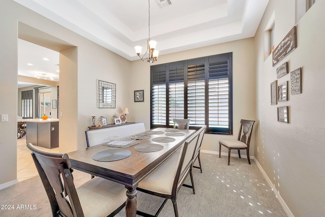 dining room with a raised ceiling, light colored carpet, and a chandelier