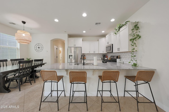 kitchen with arched walkways, appliances with stainless steel finishes, white cabinets, a sink, and a peninsula