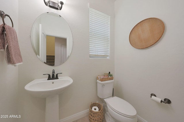 half bath with toilet, baseboards, and a sink