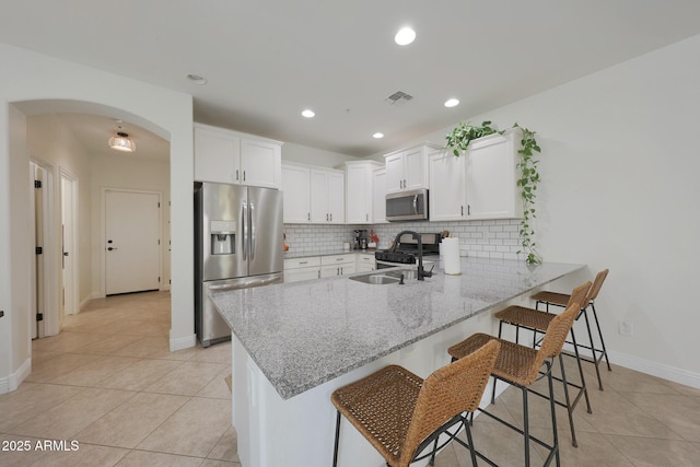 kitchen with arched walkways, decorative backsplash, appliances with stainless steel finishes, a sink, and a peninsula