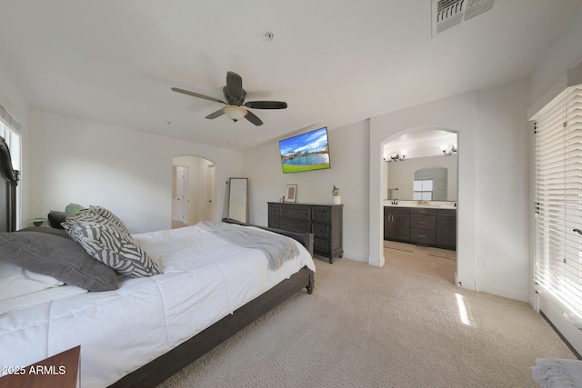 bedroom with arched walkways, light colored carpet, visible vents, ensuite bathroom, and baseboards