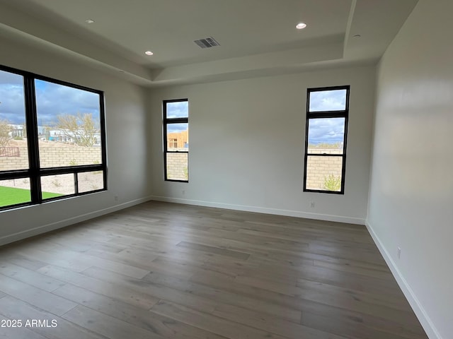 spare room featuring visible vents, a raised ceiling, baseboards, and wood finished floors