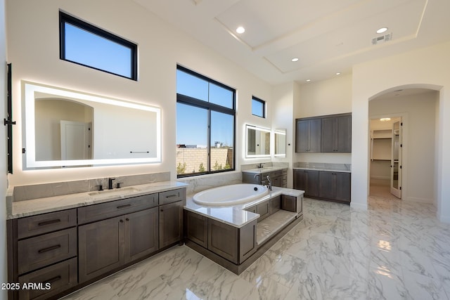 full bath with marble finish floor, a garden tub, a towering ceiling, and a sink