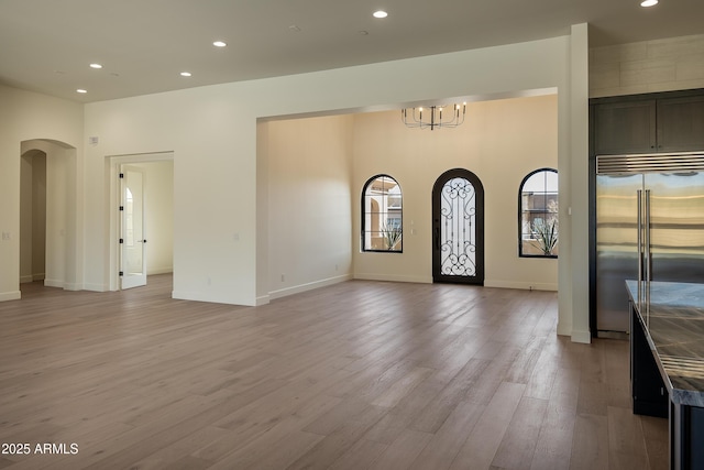 foyer entrance with recessed lighting, arched walkways, light wood-style floors, an inviting chandelier, and baseboards