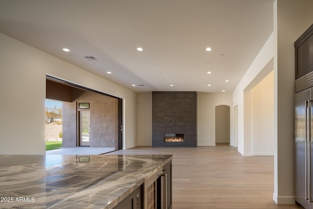 kitchen with recessed lighting, arched walkways, light wood-style floors, a fireplace, and high end refrigerator