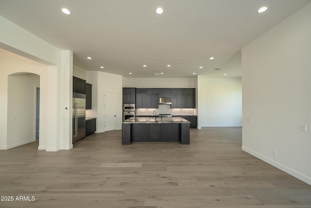 kitchen with under cabinet range hood, open floor plan, recessed lighting, stainless steel appliances, and arched walkways