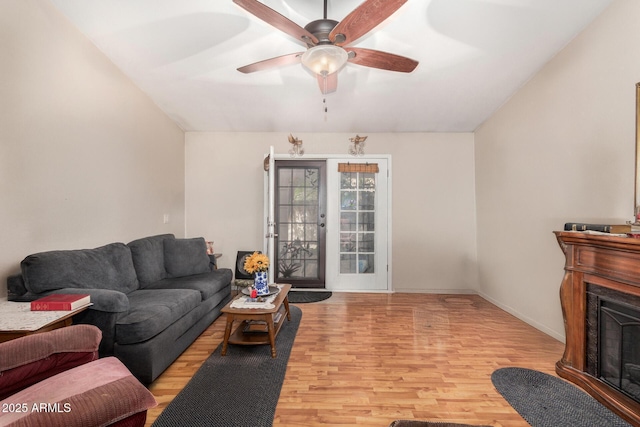 living room featuring a ceiling fan, baseboards, light wood finished floors, a fireplace, and vaulted ceiling