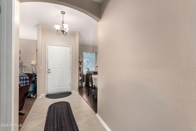 foyer featuring light tile patterned floors, a notable chandelier, arched walkways, and baseboards