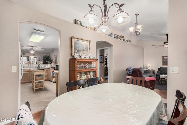 dining space with light tile patterned floors, visible vents, arched walkways, and ceiling fan with notable chandelier